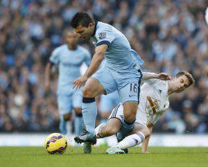 Manchester City's Sergio Aguero is challenged by Swansea City's Tommy Carroll during their English Premier League soccer match at the Etihad stadium in Manchester